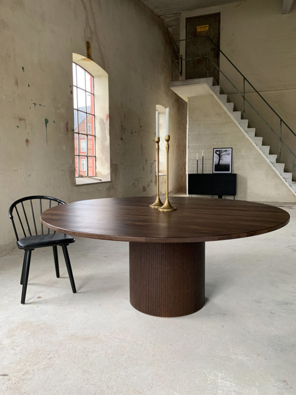 Circle dining table 180 brown stained oak An inviting & tasteful round dining table in Scandinavian design, made of solid oak, which makes the table feel genuine and authentic. The round solid dining table with extension leaves is really flexible and invites to large gatherings. Solid oak is used in the manufacture of high-quality furniture because of its durability and natural beauty. Solid oak top, solid oak & plywood columns, brown stained finish. Pillar diameter 65cm. Height 74 cm. Oak is a living material with natural movements. Over time, influenced by light & humidity, shade & maturity can change